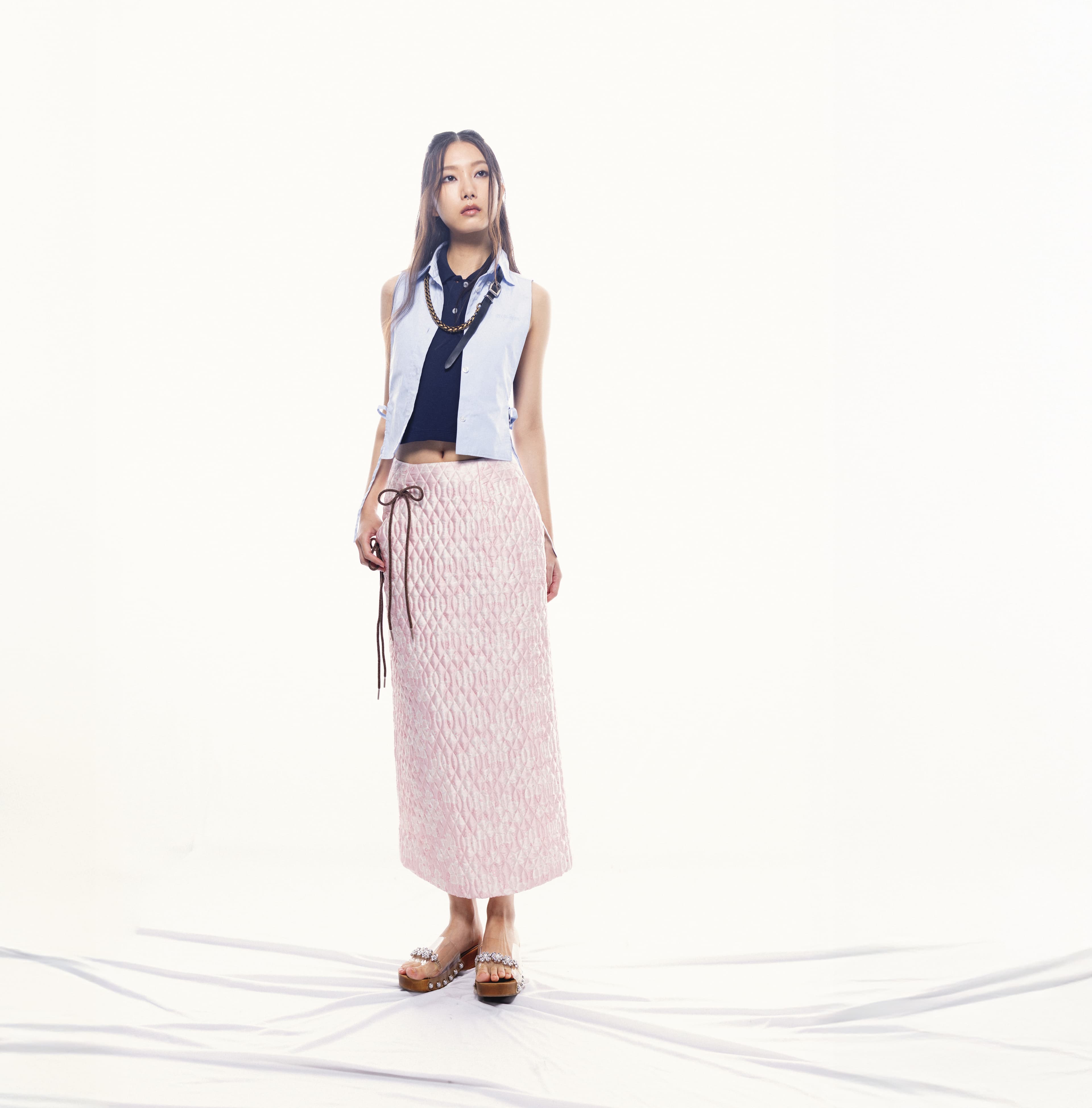 水藍背心襯衫 價格店洽 by MIU MIU；深藍背心針織上衣 價格店洽 by MIU MIU；粉色菱格不對稱鉛筆裙 NT$30,800 by Simone Rocha；珍珠裝飾透明果凍木屐鞋 NT$27,800 by Simone Rocha；皮革鍊條項鍊 價格店洽 by MIU MIU。