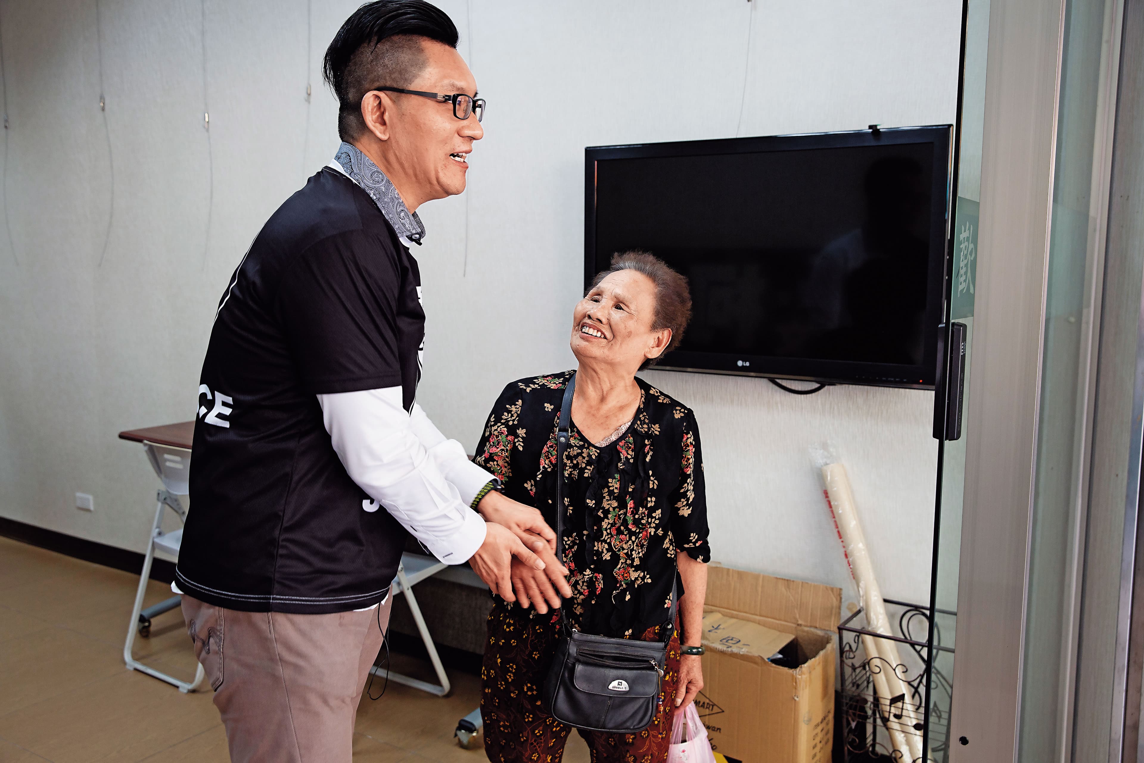 仲彥（左）轉型當網紅，服務處招牌換裝，一名70歲老婦人搞不清楚狀況，亂入表達支持，還希望他重返政壇、選立委。