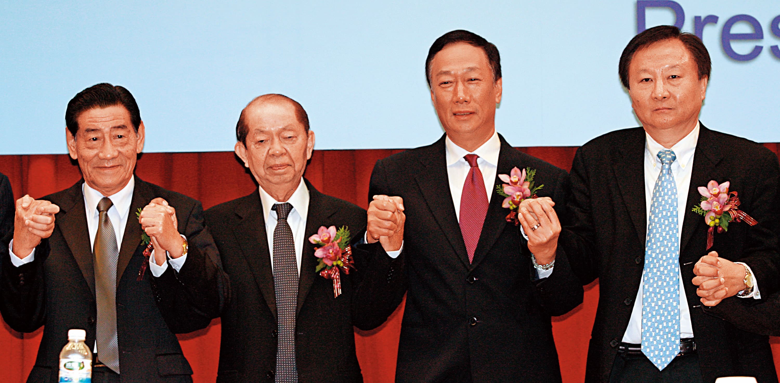 2009年鴻海董事長郭台銘（右2）手牽奇美集團創辦人許文龍（左2），宣布奇美電與群創光電合併。（中央社）