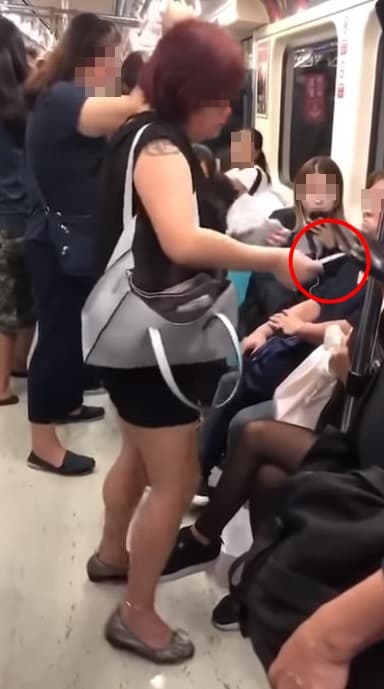黑衣女子從包包掏出粉紅色小卡，要求坐在博愛座上的金髮女子讓座。（翻攝自爆料公社）