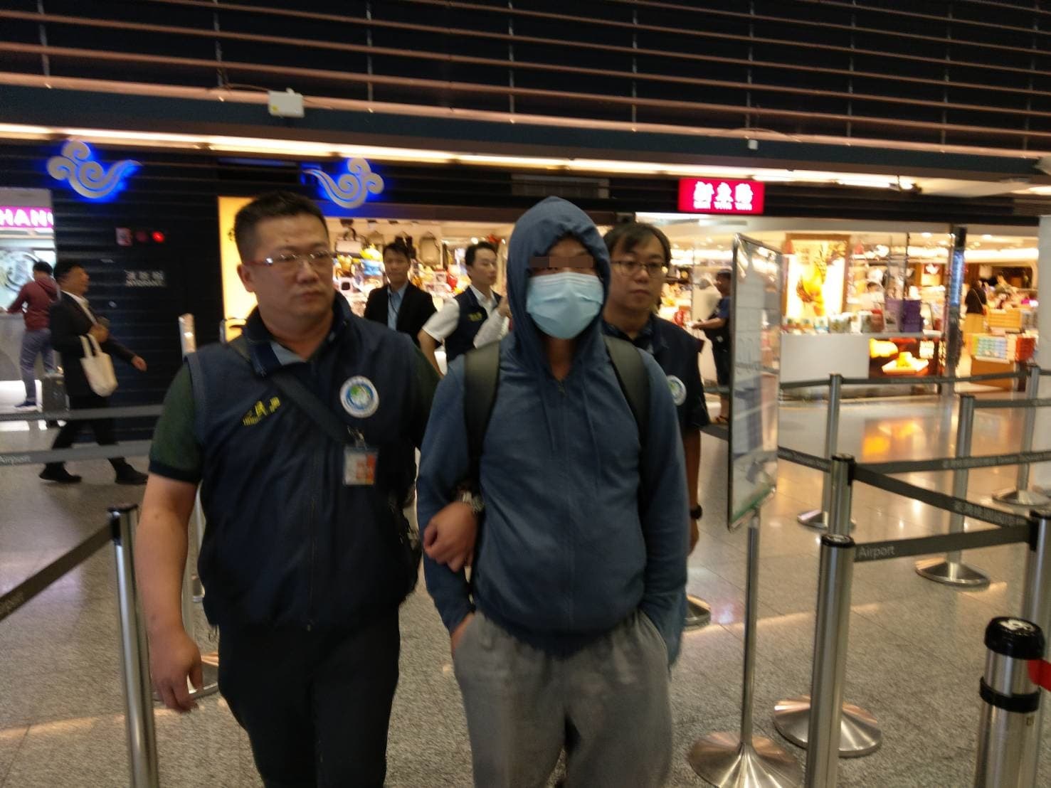 胡姓男子（戴口罩者）28日晚間遭移民署押送至機場，強制出境，並管制5年內不得再來台灣。（翻攝）