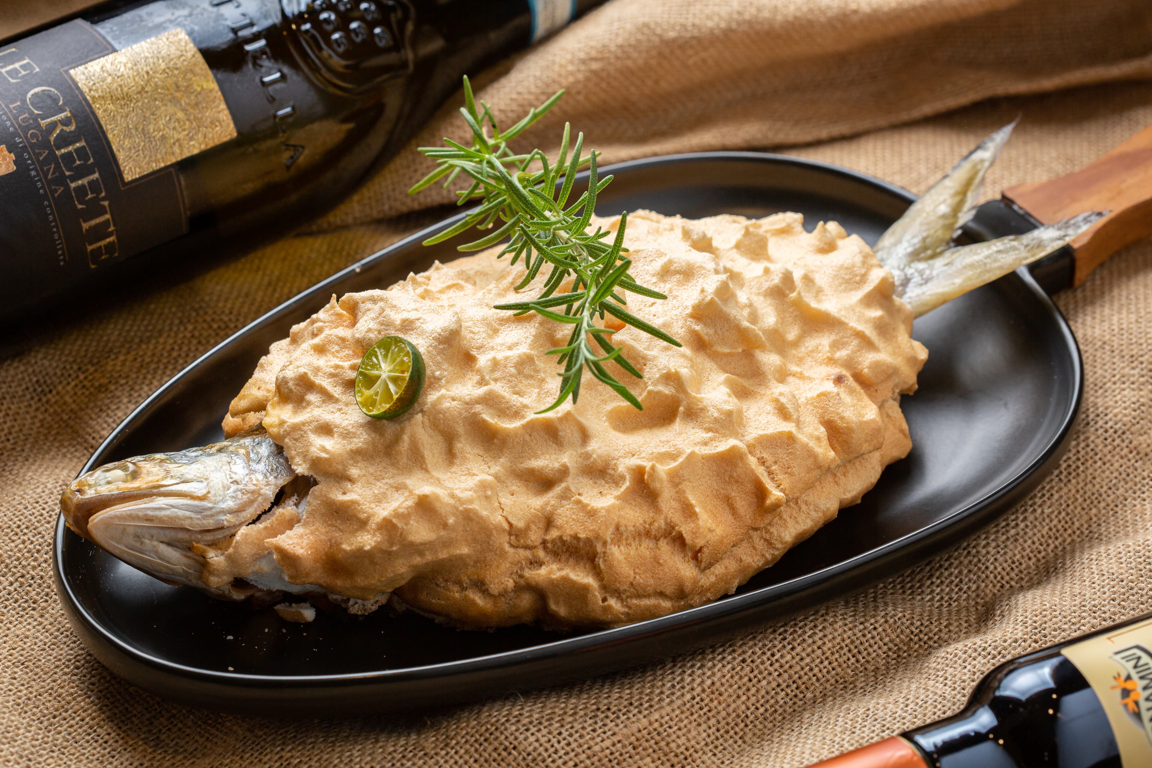 掀開「地中海香料烤魚」的鹽焗外殼，細嫩緊實魚肉沁出鮮美湯汁（780元／份），搭上「Le Creete Lugana DOC」柑橘系果香進一步提升鮮美。（6,000元／6瓶、箱）