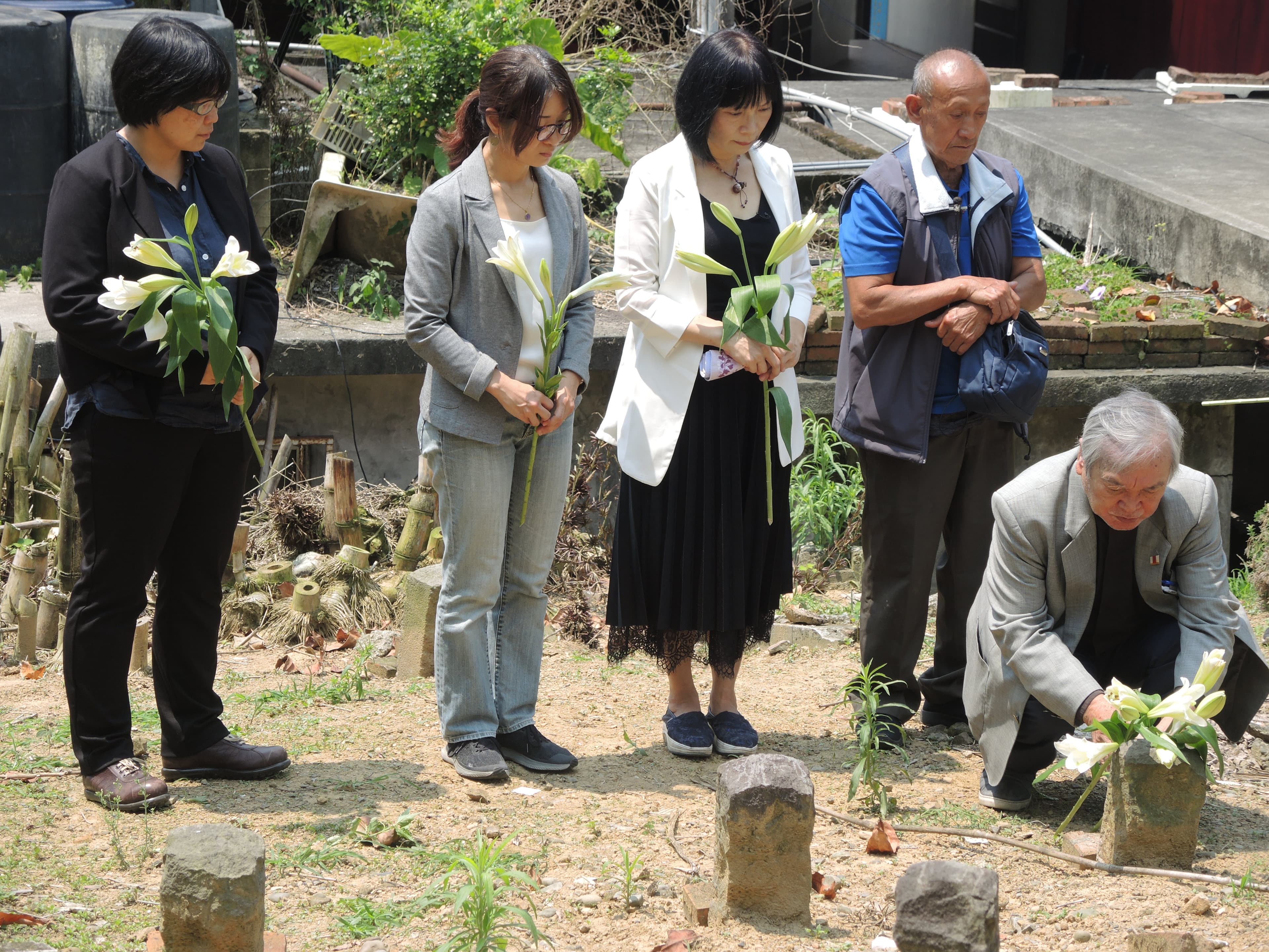 促轉會主委楊翠（左3）、彭仁郁委員（左2）、副主委葉虹靈（左1）、牧師伍錐（右1），陪同布農族原住民伍金山（右2）到六張犁政治受難者的亂葬崗，挖掘父親伍保忠的遺骨。（促轉會提供）