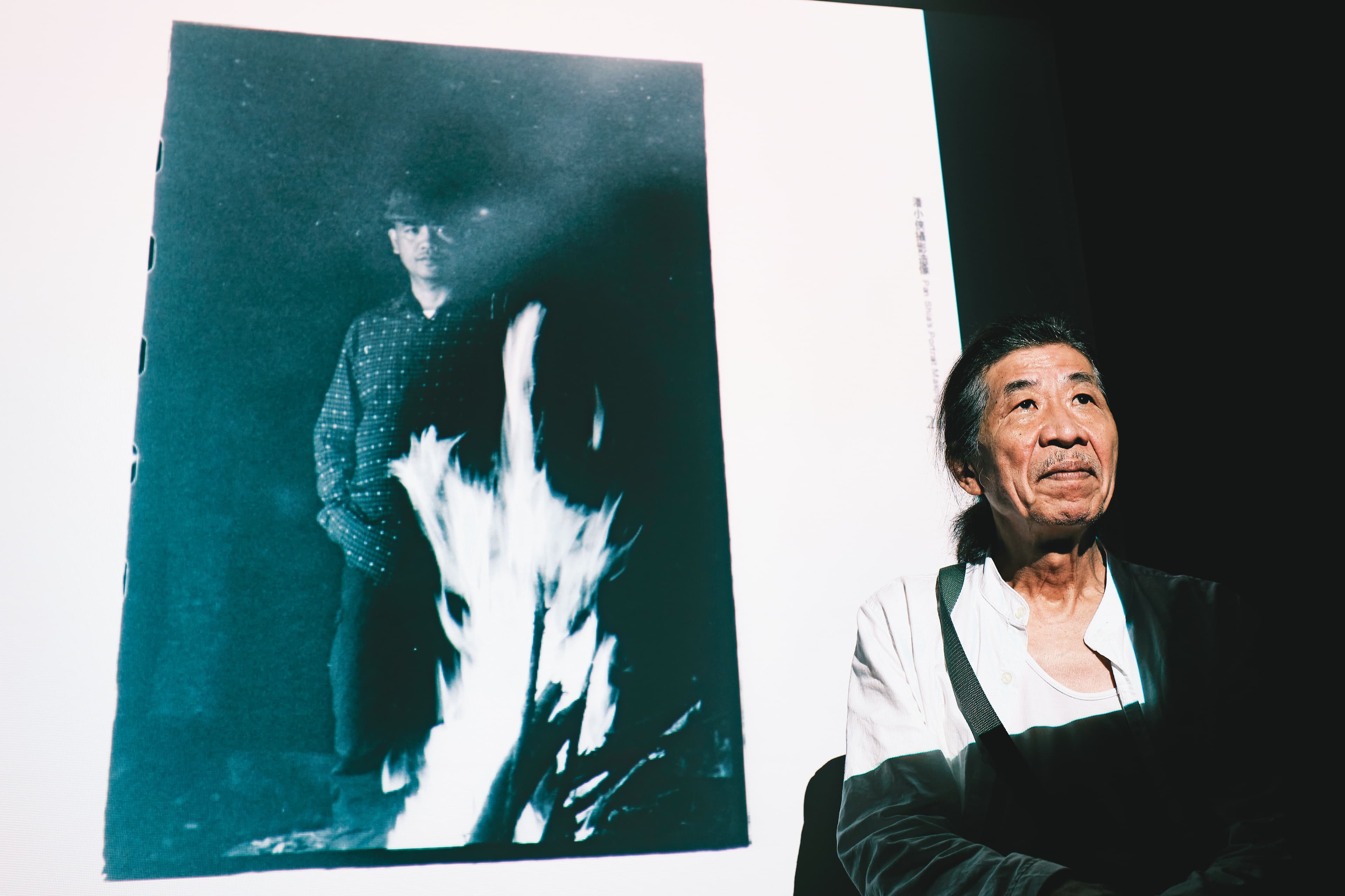今年潘小俠出版《台灣作家一百年》，7月以原住民作家為主題開座談會。背景圖片為他拍攝的布農族作家乜寇‧索克魯曼，他說自己當天到達部落時已夜深，於是藉燃燒柴火的光線拍照。