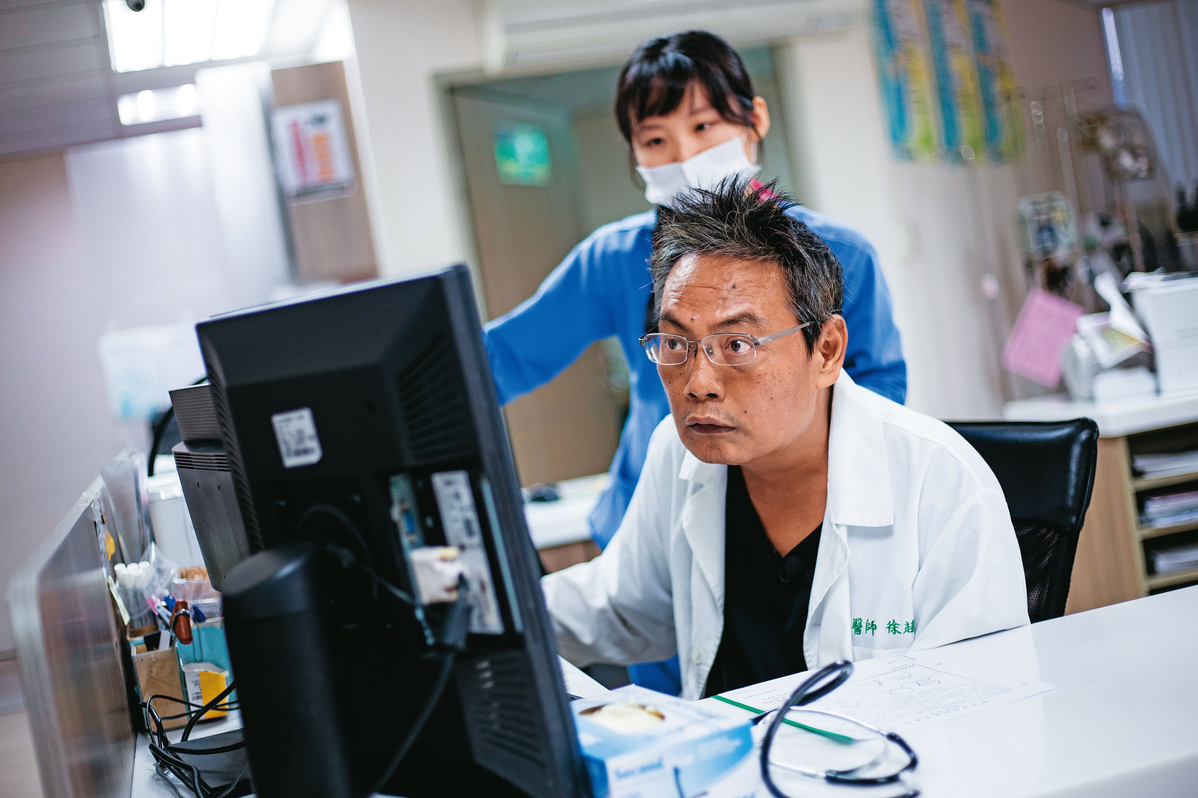 徐超斌（前）現於台東醫院工作。他看診時只能以單手打字、行動也不甚敏捷，但他說從未遇過病人不耐，共事的醫護相處也十分融洽。