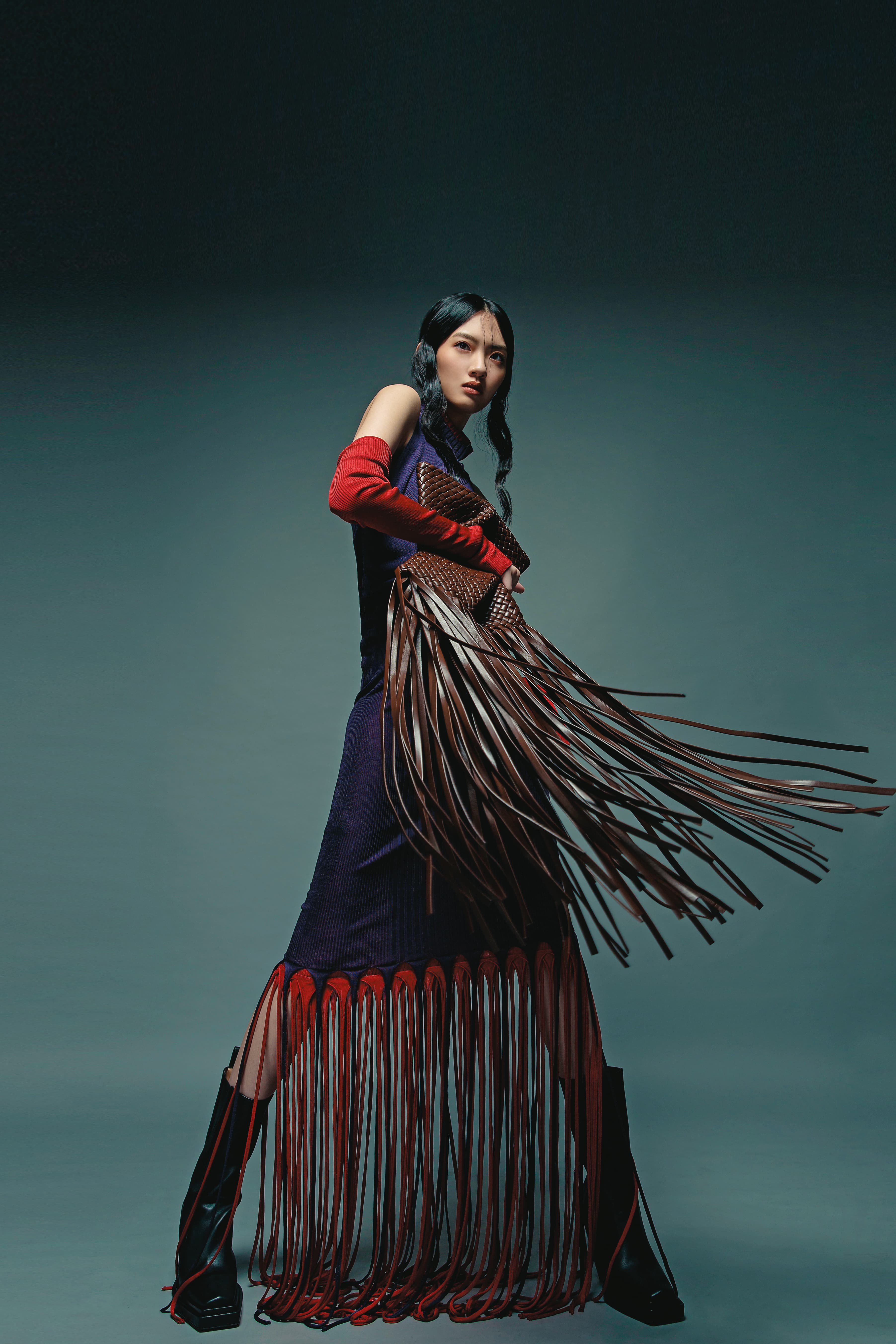 午夜藍、猩紅色層次流蘇洋裝 NT$128,100 by BOTTEGA VENETA／Lean小牛皮切爾西高跟靴 NT$49,300 by BOTTEGA VENETA／Crisscross編織小羊皮流蘇手拿包 NT$142,900 by BOTTEGA VENETA