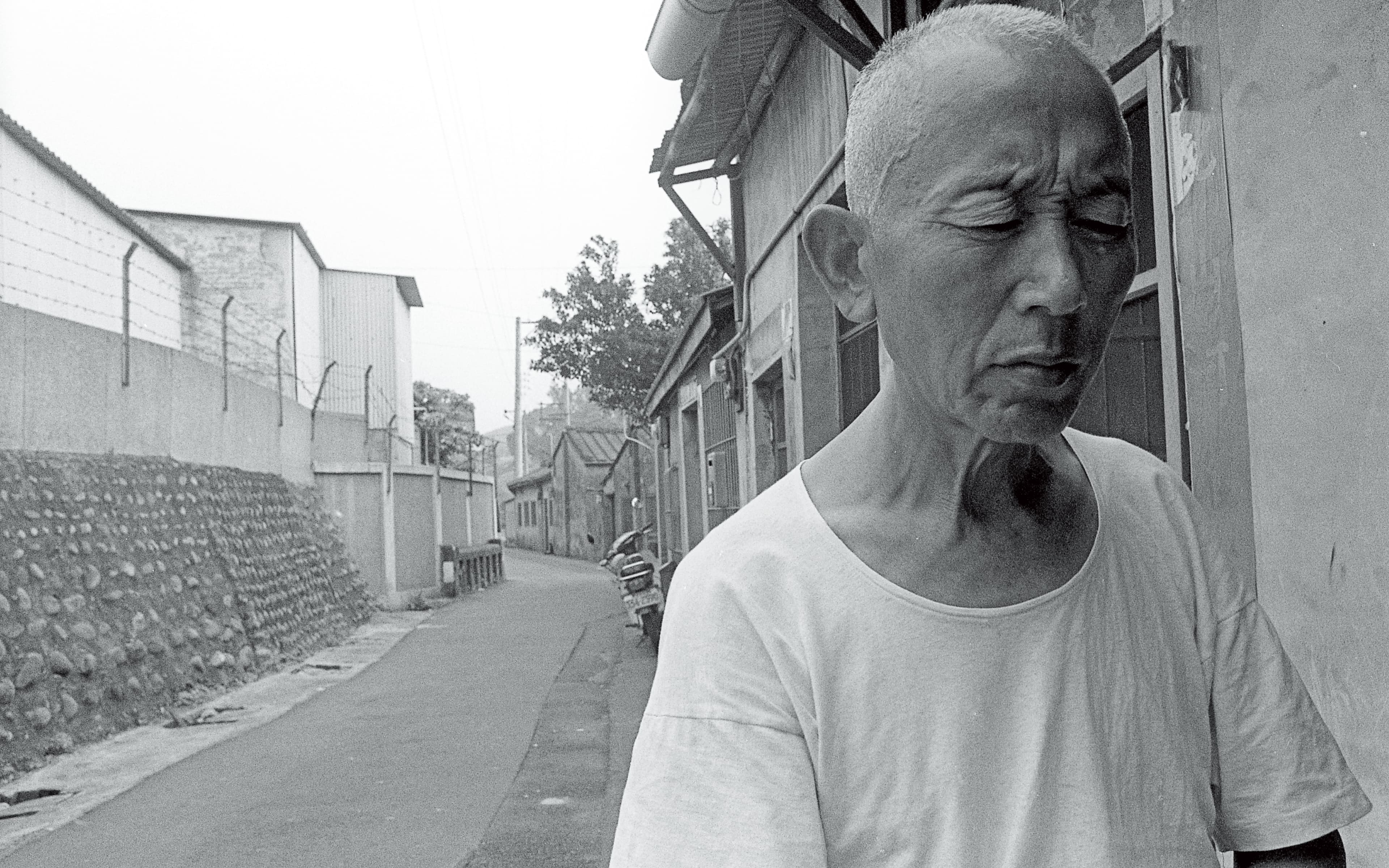 周子飛當年被救出後，媒體在張雄家門口拍攝張雄（圖）。時移勢易，周子飛如今對照片左方那面石牆仍有印象。（蔡明德攝）