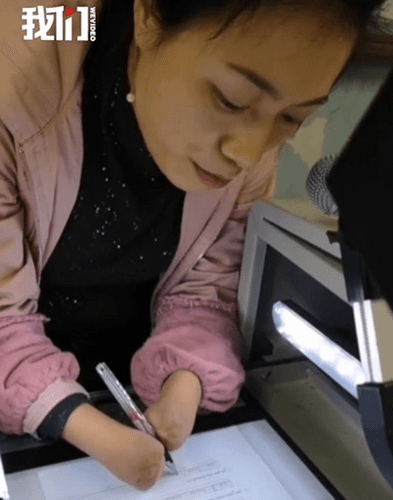 杜宣梅平時寫字需要用雙臂夾著筆，若要打開投影機則用雙臂夾著長棍開啟開關。（翻攝自新京報我們視頻）
