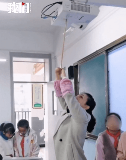 杜宣梅平時寫字需要用雙臂夾著筆，若要打開投影機則用雙臂夾著長棍開啟開關。（翻攝自新京報我們視頻）