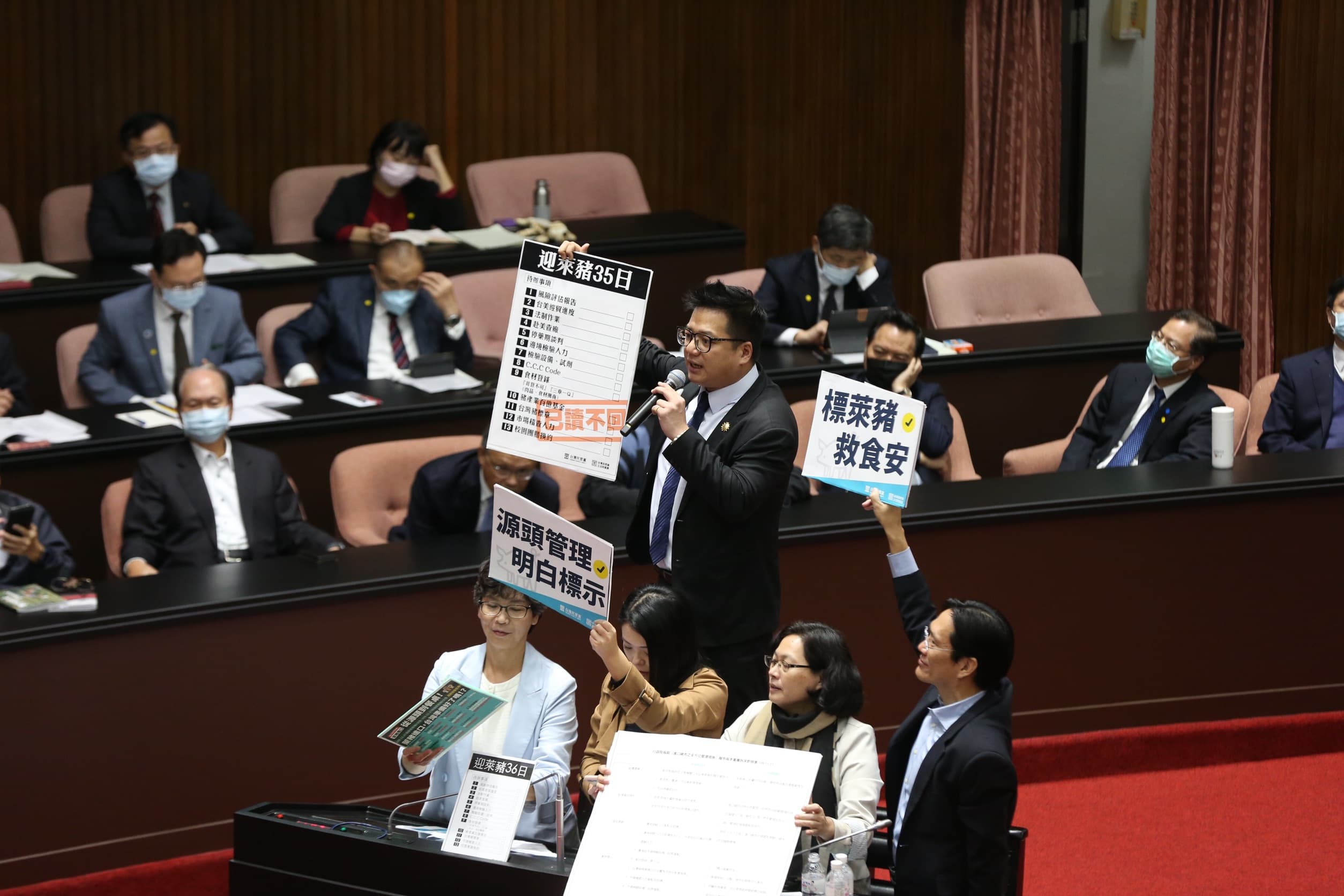 民眾黨立委邱臣遠（舉「迎萊豬35日」板者）質詢時，同黨立委在旁協助。