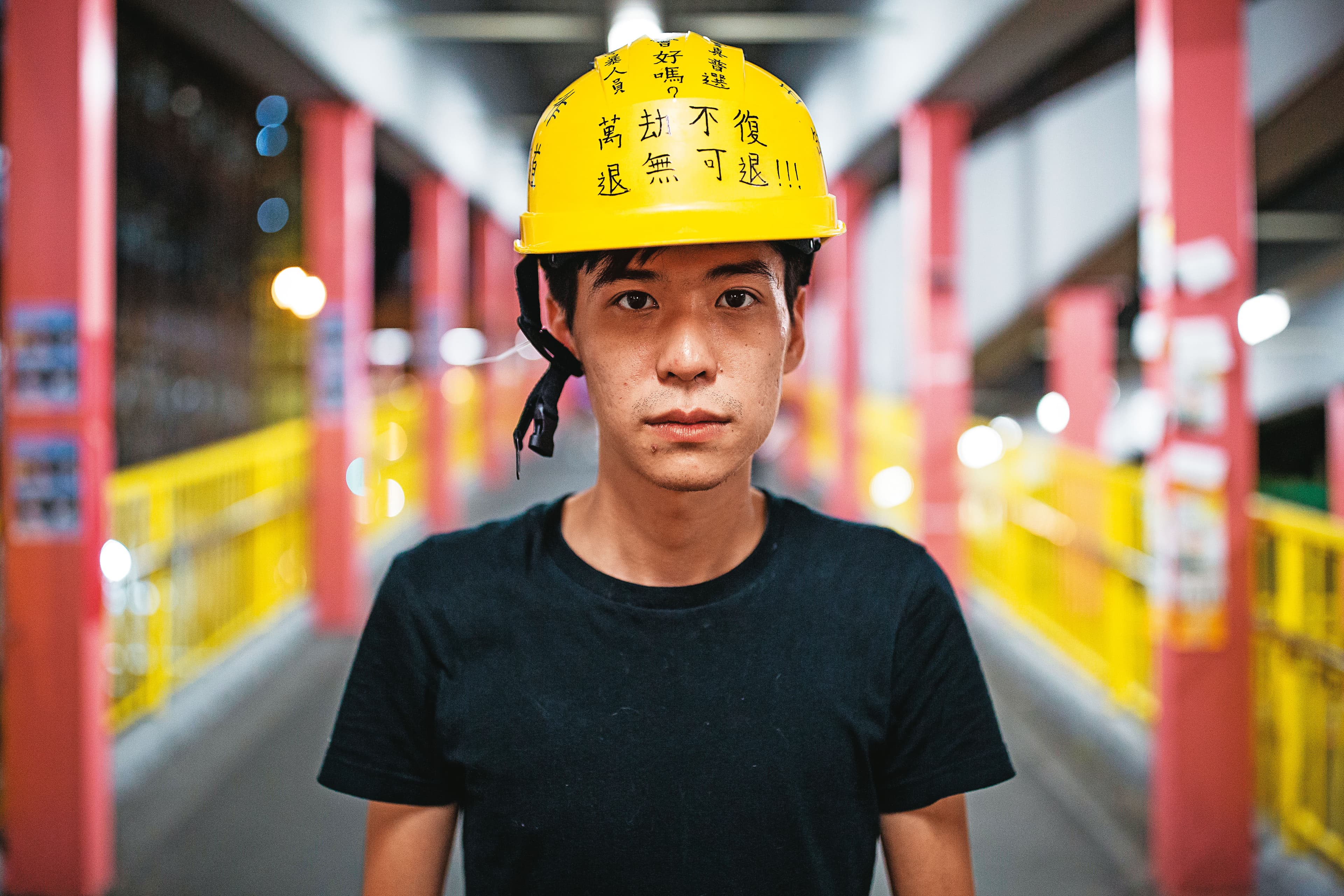 2019年反修例運動期間，岑敖暉接受本刊專訪後站在一處地鐵站拍照，頭上安全帽寫著抗爭標語。