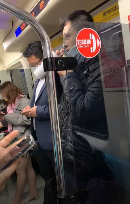 一名身穿黑色外套男子在捷運車廂內拉下口罩狂喝飲料。（讀者提供）