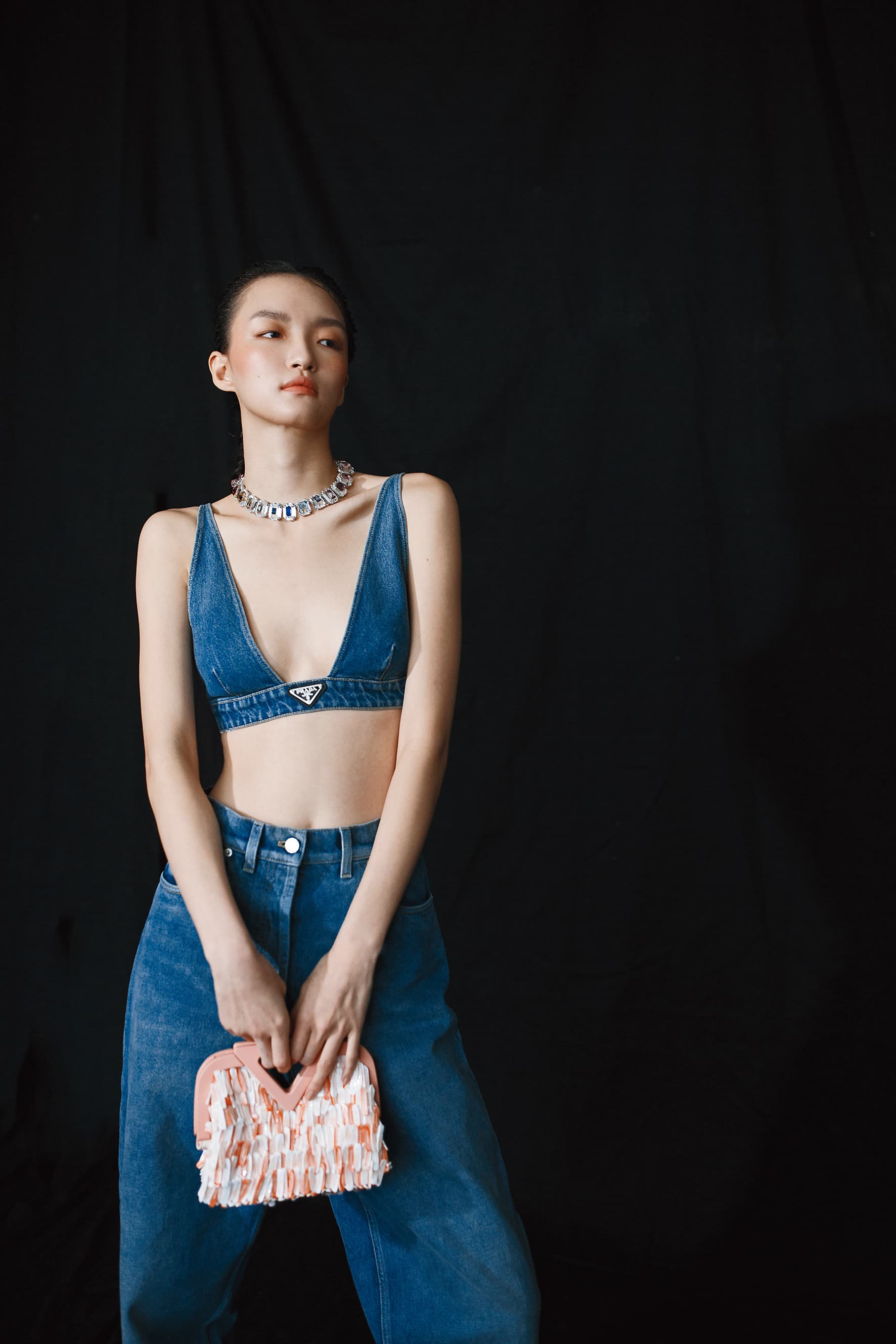 馬卡龍粉鳳凰螺貝殼手提袋 NT$196,200 by BOTTEGA VENETA；有機丹寧背心 NT$17,000 by PRADA；有機直筒牛仔褲 NT$31,500 by PRADA；Chroma頸鍊 NT$31,900 by SWAROVSKI。