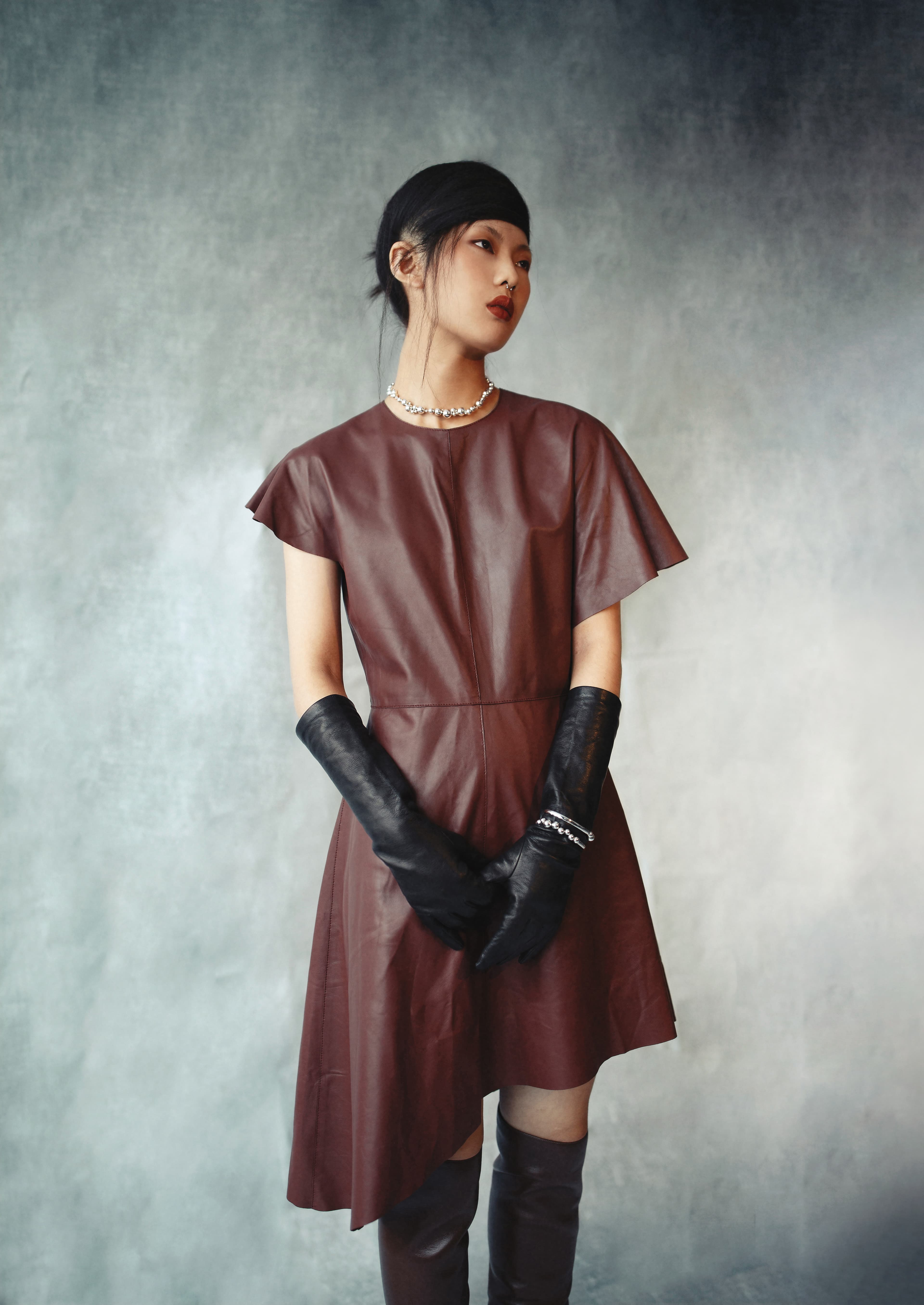 不規則剪裁洋裝  價格店洽by LOEWE；MOSTRA深栗色高跟長靴 價格店洽by BOTTEGA VENETA；那帕羊皮手套  價格店洽 by BOTTEGA VENETA；MOONLIGHT GRAPES系列純銀葡萄鎖骨鍊 NT$32,500 by GEORG JENSEN；MOONLIGHT GRAPES系列純銀手鐲 NT$18,500 by GEORG JENSEN