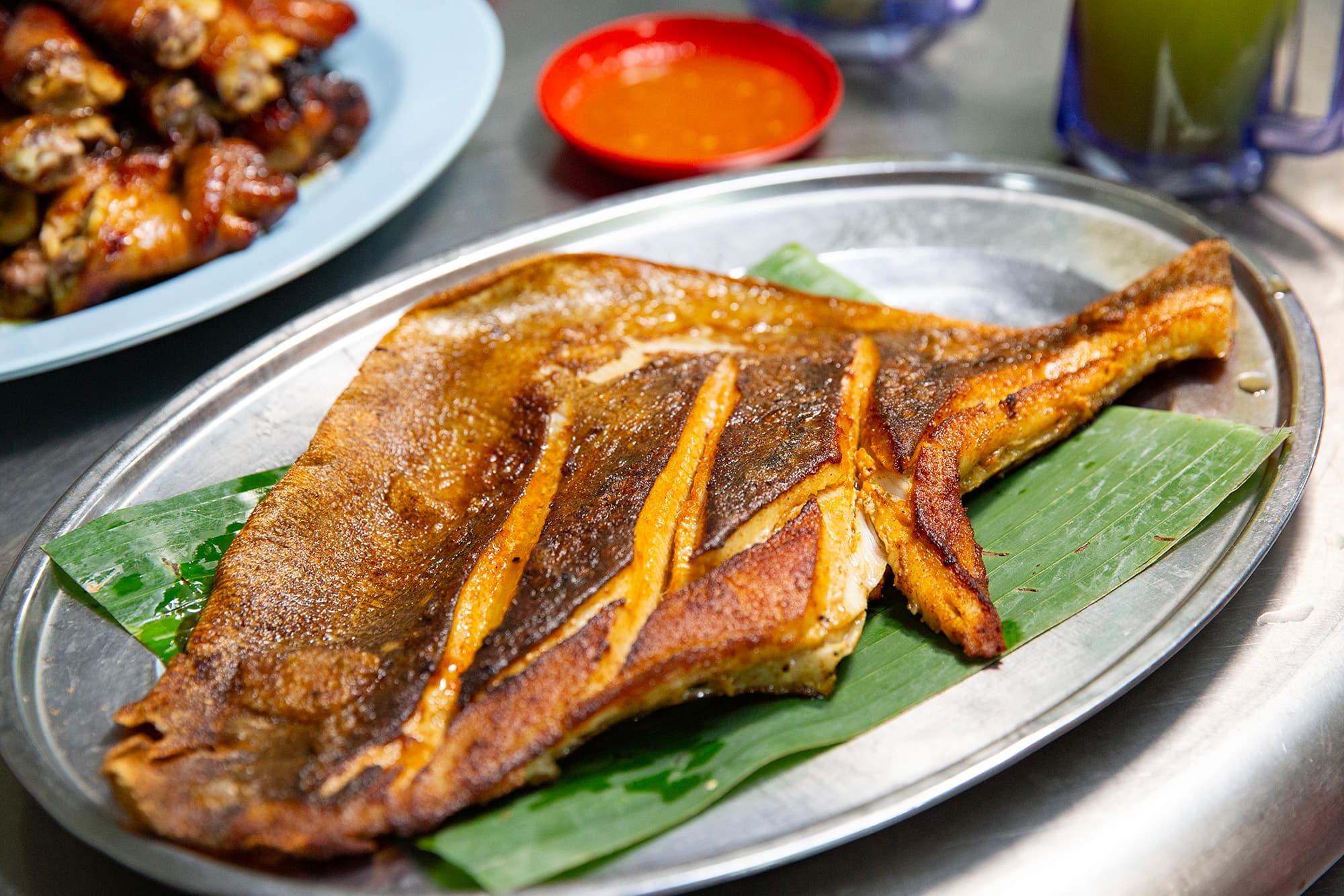 黃亞華的「燒蒲魚」選用新鮮魔鬼魚，裹上特製叁巴醬後以香蕉葉包裹炭烤，魚肉嫩滑多汁，帶有濃郁的辣香與炭火味。