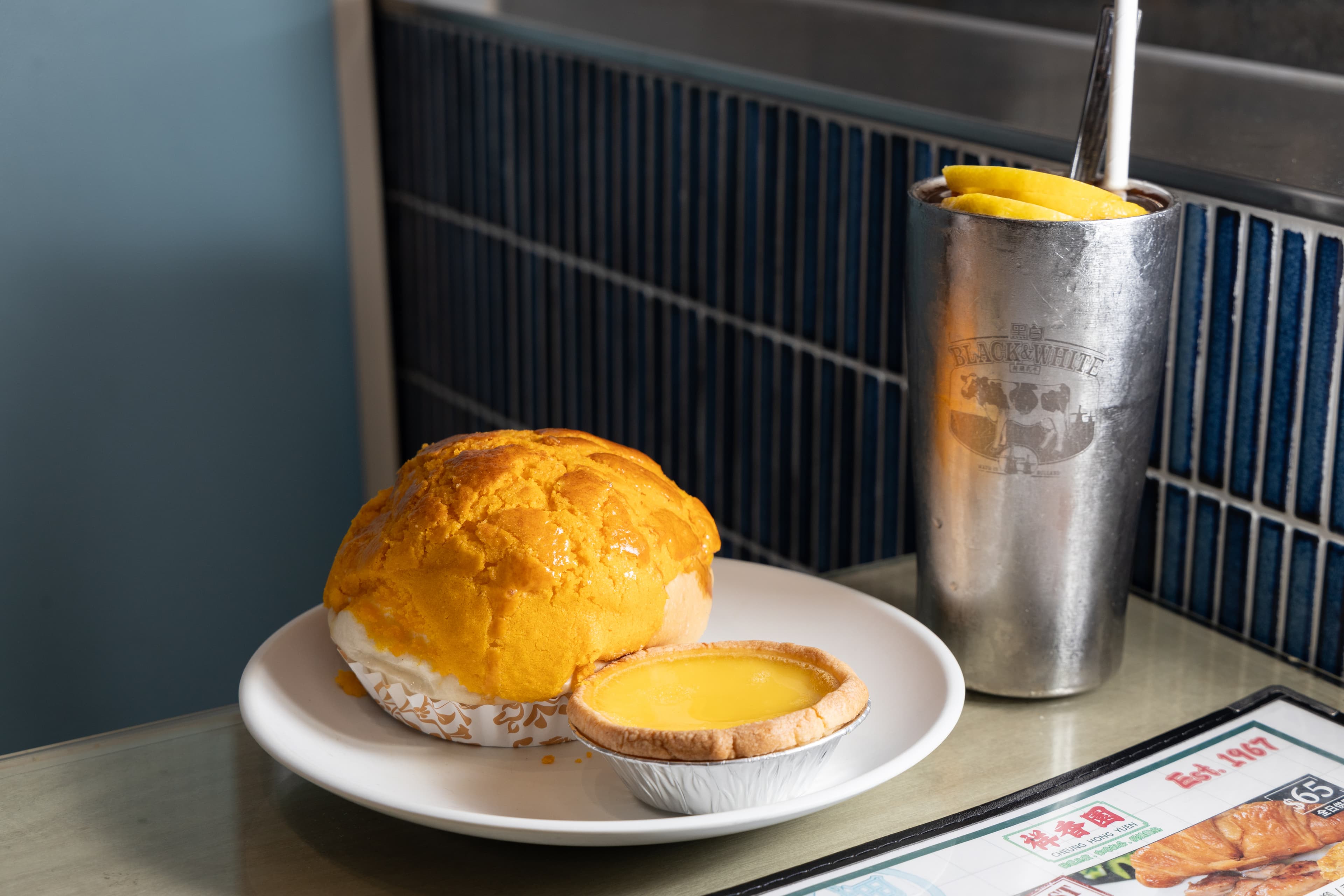 鎮店三寶之一的「菠蘿包」（後，港幣10元／個，NT$41）與「港式蛋撻」（前，港幣9元／個，NT$37）配上清爽的「凍檸茶」（右，港幣23元／杯，NT$94）。