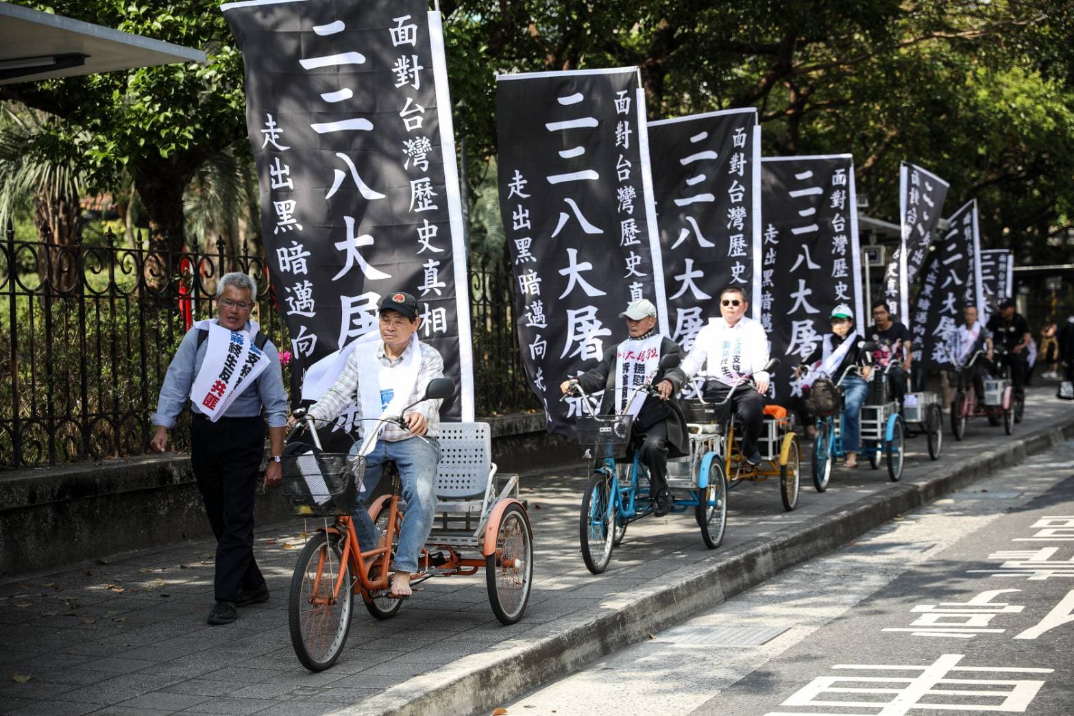 228事件78週年追思會，抗議團體在腳踏車上插著大大的「二二八大屠殺，面對台灣歷史真相，走出黑暗邁向光明」黑底白字布條。