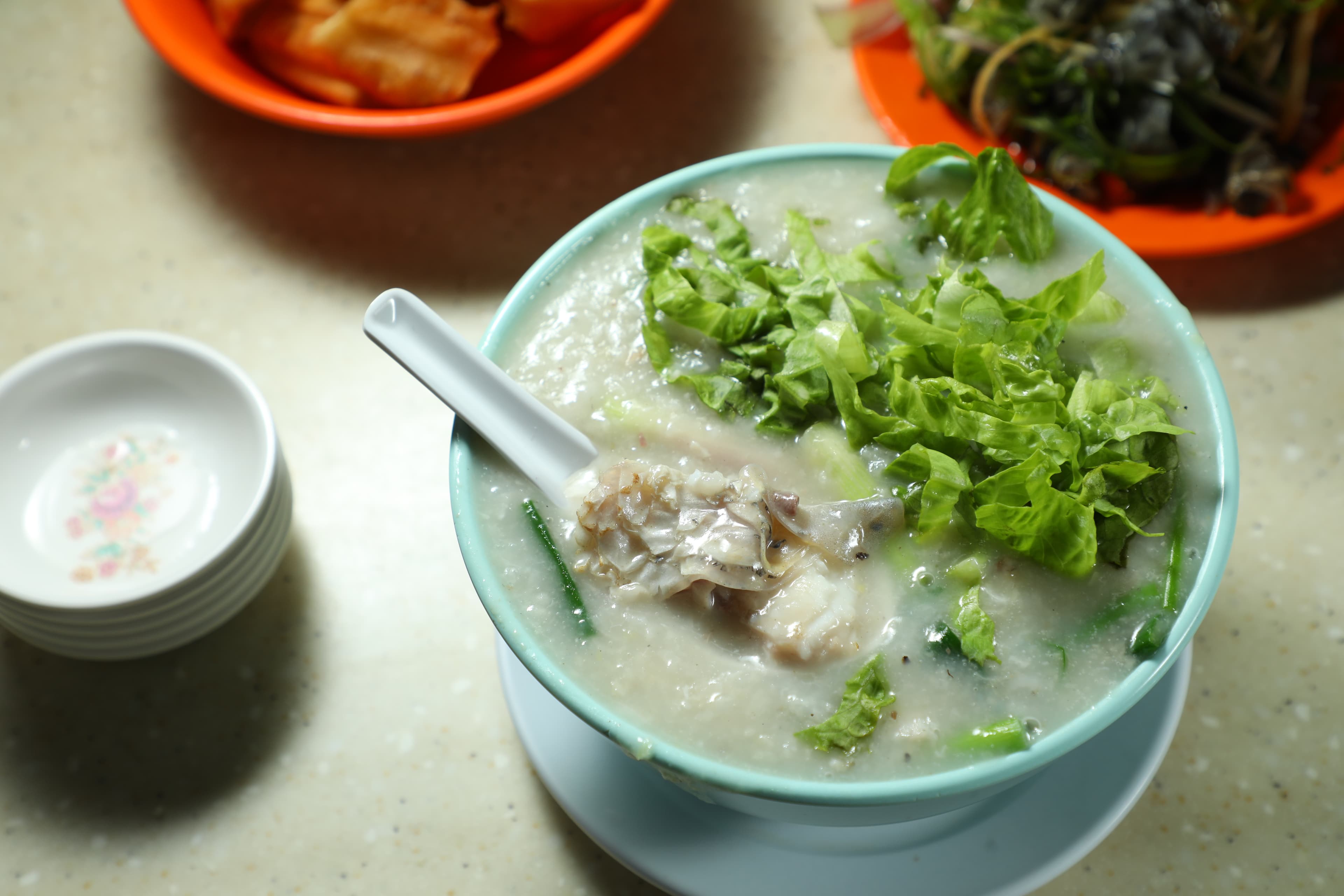 「魚腩粥」（前，港幣50元／碗）的粥面鋪滿生菜，能嘗到軟嫩魚肚，也可加點「油條」（後，港幣11元／份）來搭配。