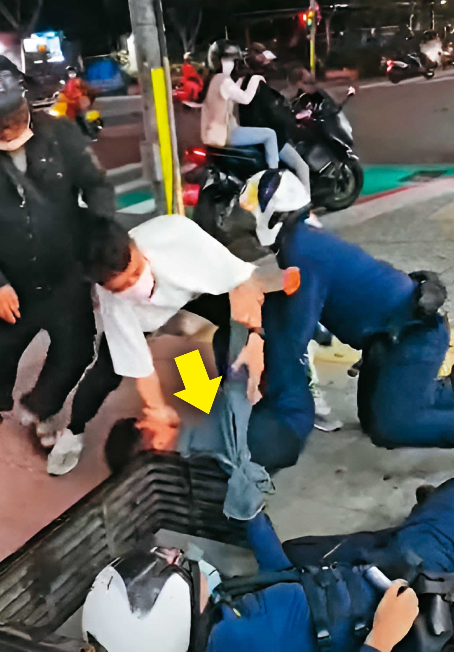 黃先生（箭頭處）被員警推倒在人行道上，一旁的民眾也上前協助員警逮人。（翻攝畫面）