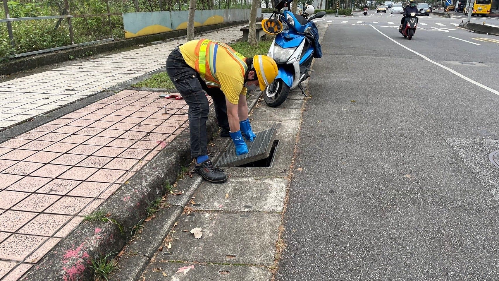 清潔隊員戴上橡膠手套，打開水溝井蓋尋找民眾掉落的失物。（北市環保局提供）